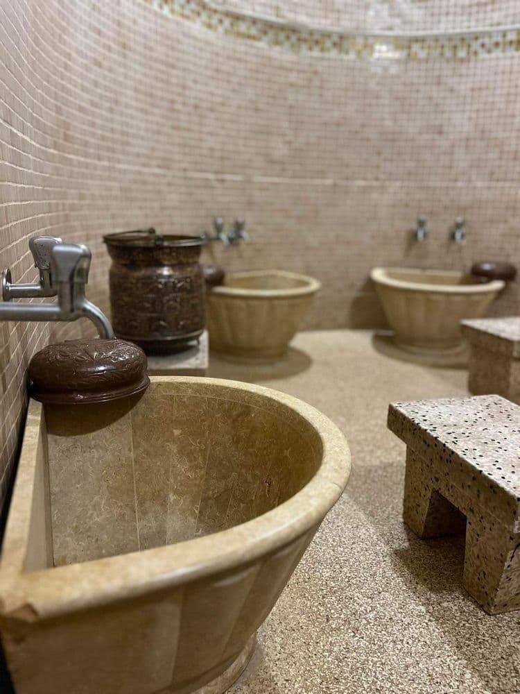 Hammam algérien traditionnel avec bassines en pierre, robinetterie simple et espace de bain authentique